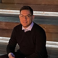 Person wearing glasses and a black sweater, seated on wooden steps outdoors.