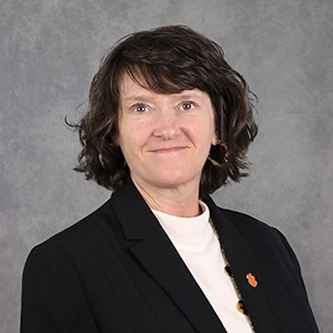 Professional headshot of a woman with curly hair wearing a black blazer and a white shirt.