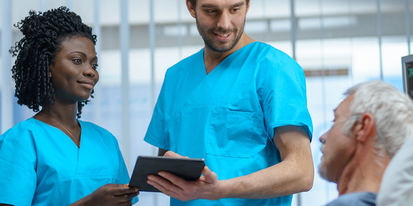 Two people in scrubs talking with patient in hospital bed.