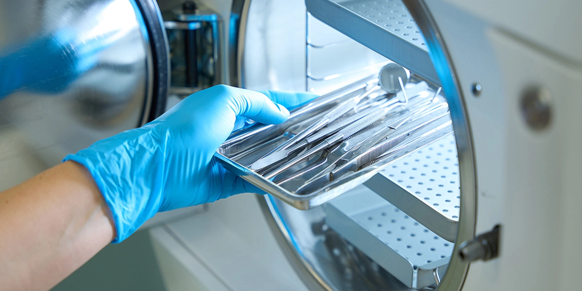 Gloved hands placing sterile surgical instruments into machine.