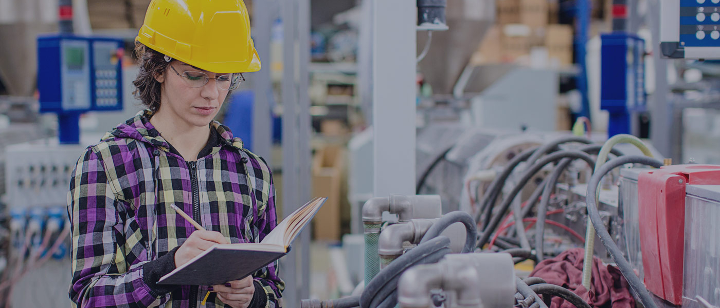 Woman in hard hat in factory taking notes