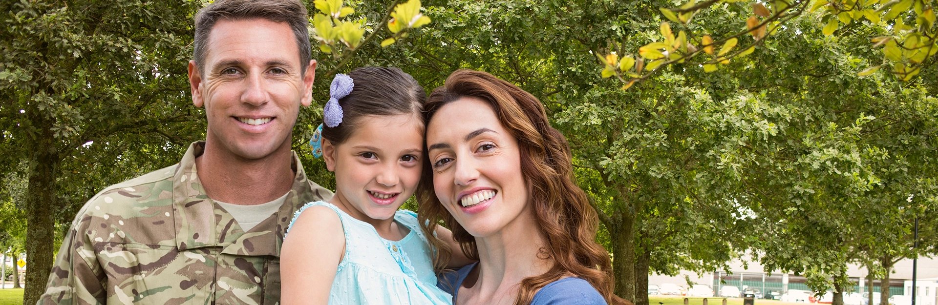 Man in army uniform with woman and child in outdoor setting.