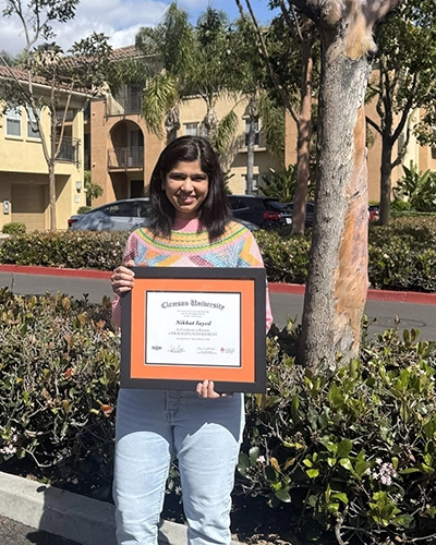 Person standing outdoors holding a framed Claremont University diploma.