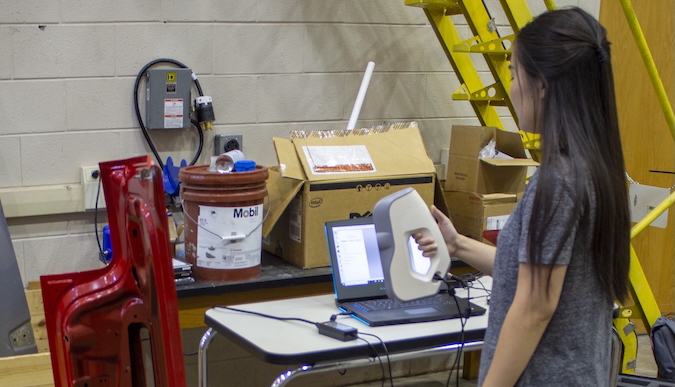 Dora Yang using the 3D scanner to scan a hail dented sheet of metal.