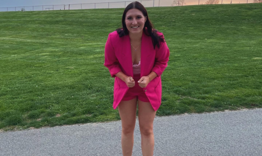 A young woman in a pink suit smiles at the camera.
