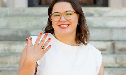 A smiling young woman in a white shirt holds up her Clemson ring.