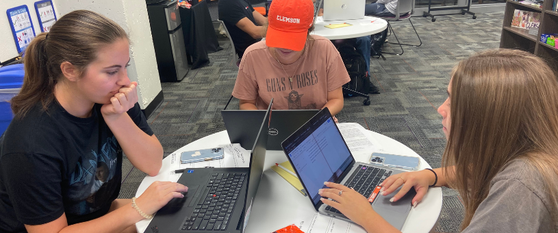 Three students sit at a table working on their writing projects.