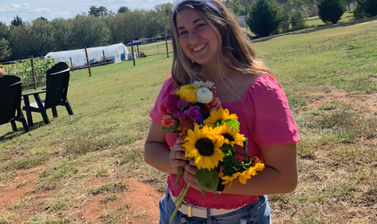 A young woman with brown hair holds a bouquet of flowers.