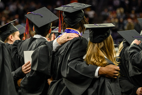 The back of four graduates with their arms draped over each others shoulders.