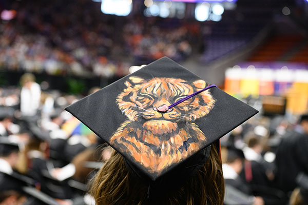 Student wearing a graduation hat with a realistic tiger face with squinting eyes painted on top.