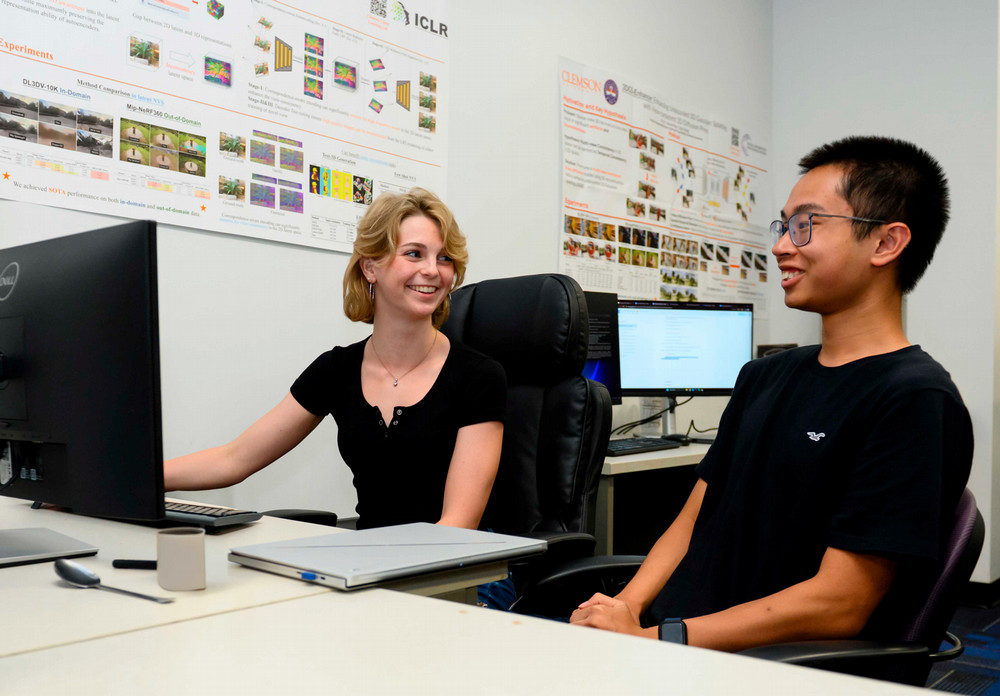 Two students sitting at a desk and talking about content they are seeing on a computer screen in front of them.