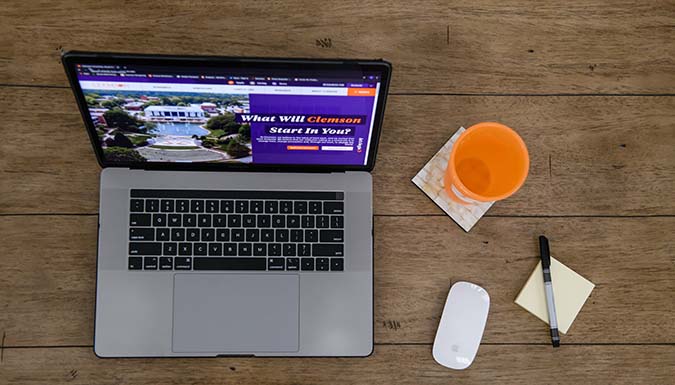 A laptop, mouse, cup and notepad on a desk