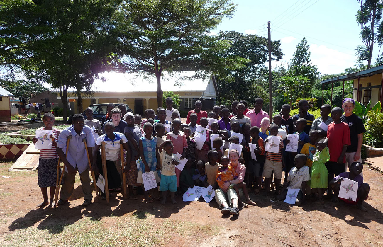 A student standing outside with a group of schoolchildren and a teacher in Africa.