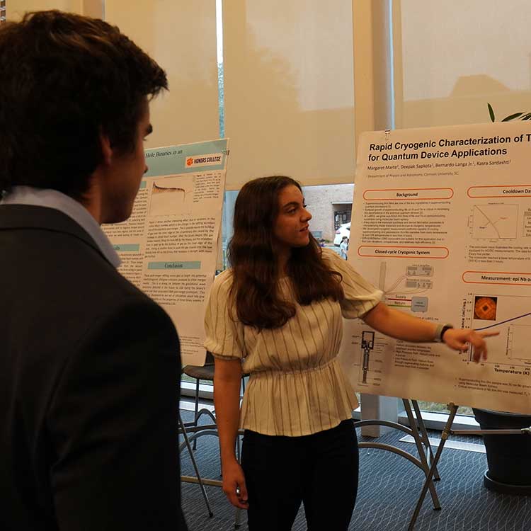 An Honors student standing in front of a research poster she developed. She is discussing her research with a Clemson faculty member.