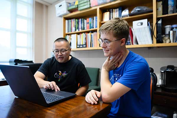 A professor and student talking while looking at a laptop