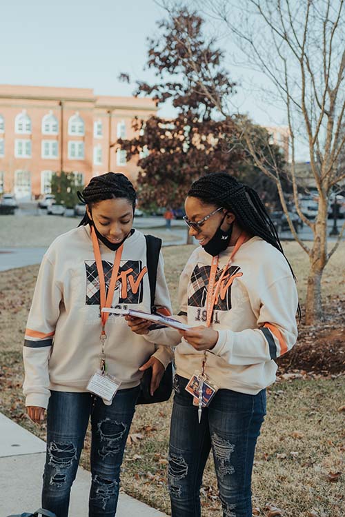 Twins standing on campus and looking at a booklet.
