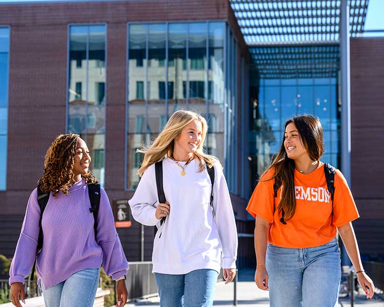 Three female students walking, talking and smiling on Clemson University campus. 