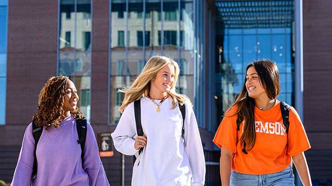 Three female students walking, smiling, and talking together on campus.