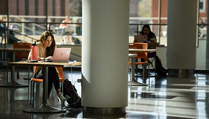 A student working on her laptop at a table.