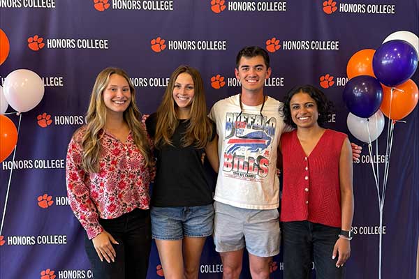 four students standing together and smiling in front of an Honors College backdrop