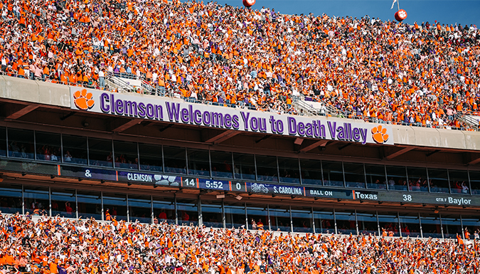 A packed Memorial Stadium during a home football game with the words 'Clemson Welcomes You to Death Valley' showing on the facade of the upper deck.