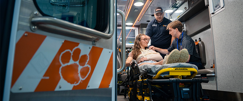 A pre-hospital education student practices applying a sling to a fellow student as an instructor provides direction.