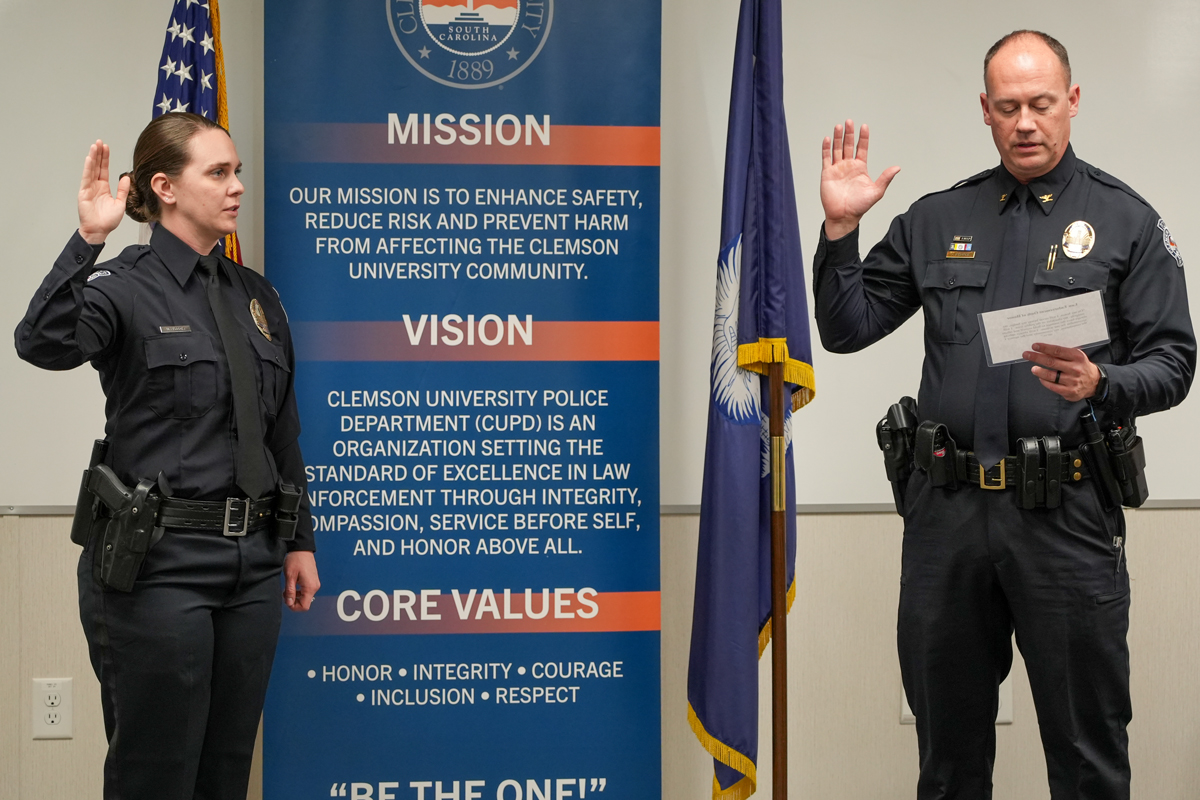 Two police officers take an oath during a swearing-in ceremony in front of a mission and core values banner and U.S. and state flags.