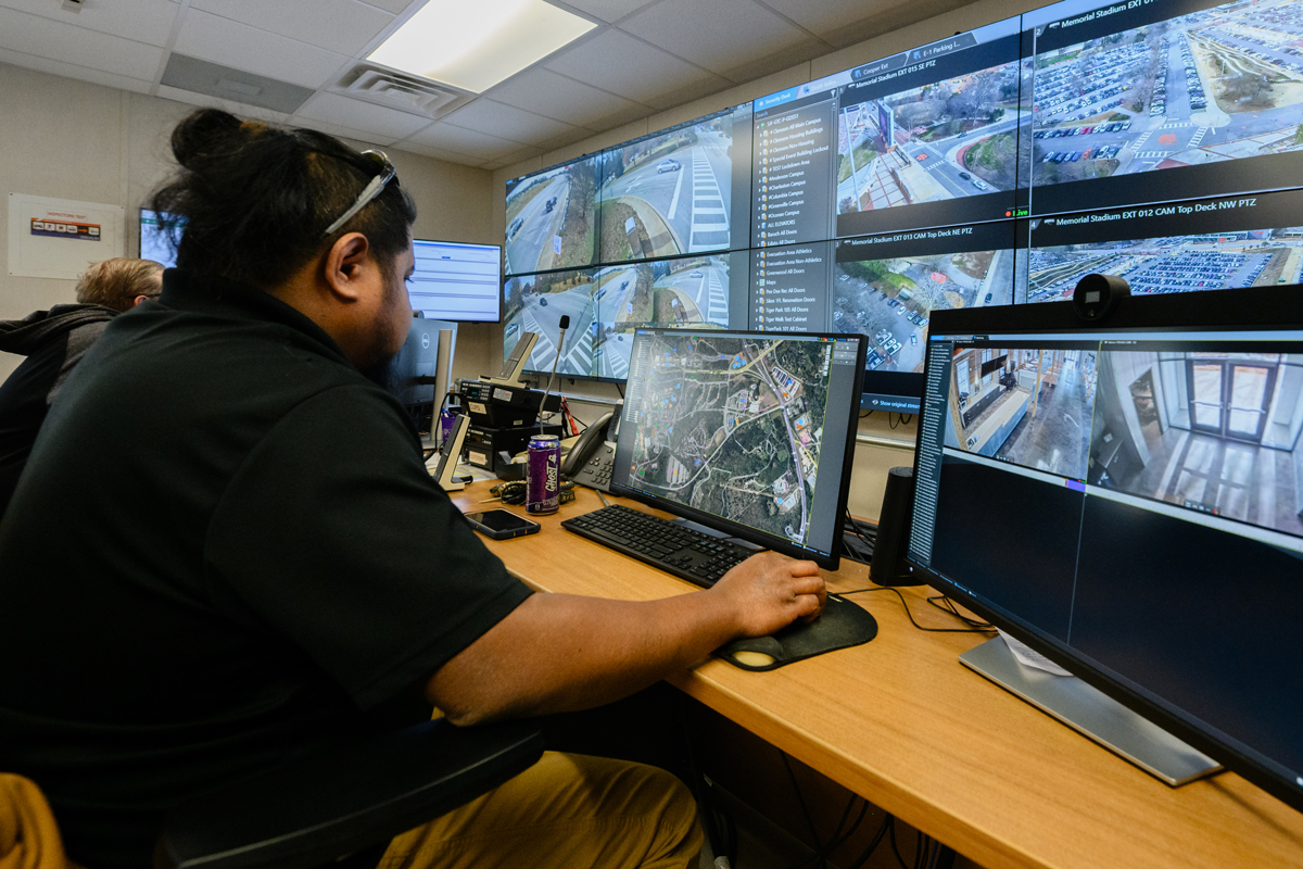 Security operations staff monitoring multiple surveillance camera feeds on a video wall and desktop monitors.
