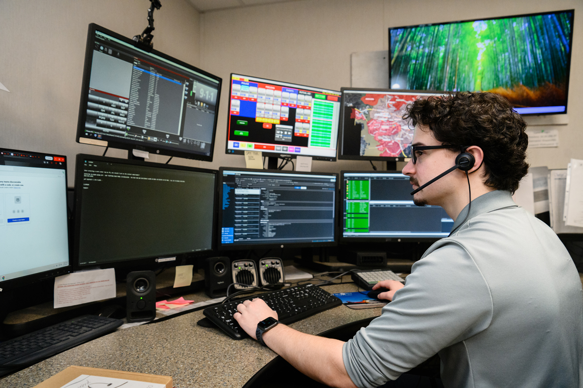 Call center operator wearing a headset monitors multiple computer screens in a control room.