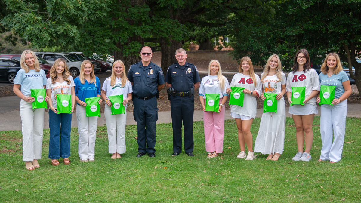 Group of women holding green gift bags standing outdoors with two police officers in uniform.
