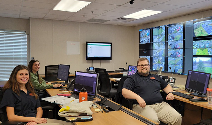 Three workers sit in front of computers and a wall of monitors