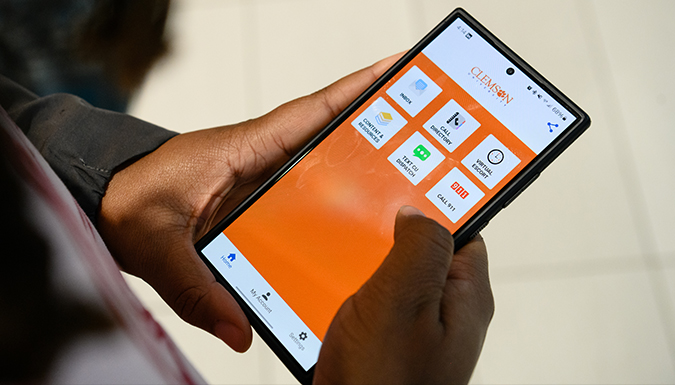 A student holds a smartphone with the Rave Guardian app showing on the screen.