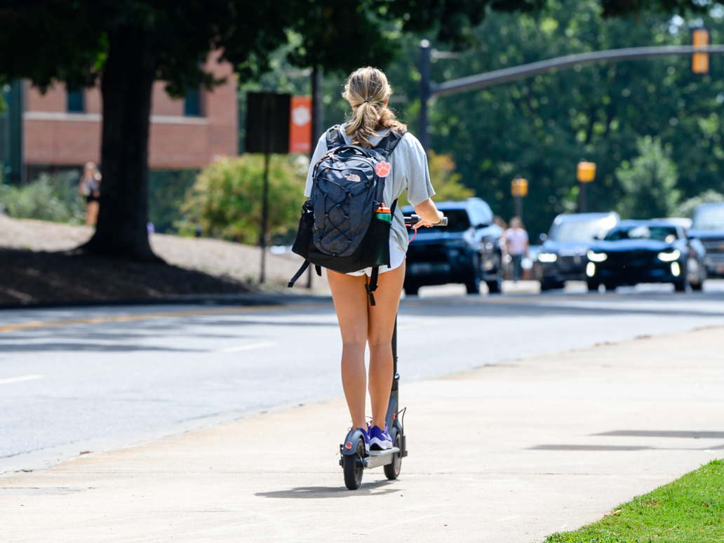 A student rides an e-scooter on the sidewalk