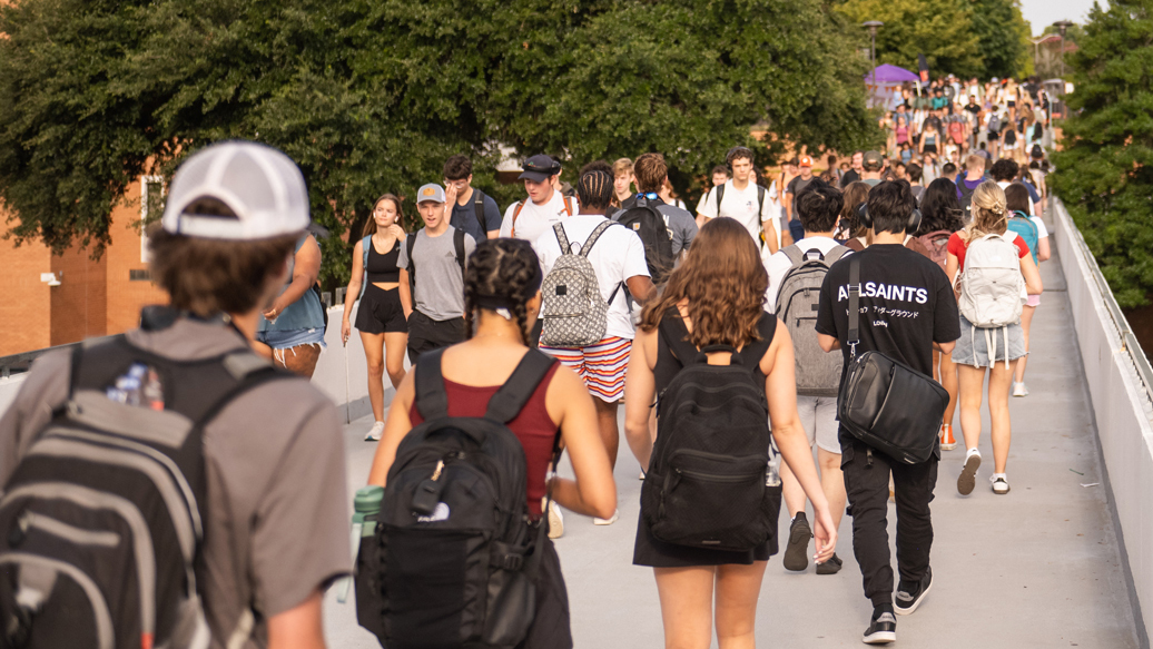 Student walking on library bridge on a warm day