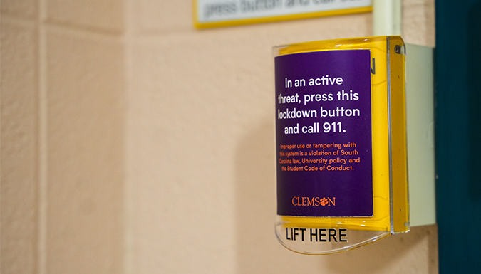 A yellow lockdown button in one of Clemson's classrooms with a sticker that reads In an active threat, press this lockdown button and call 911.