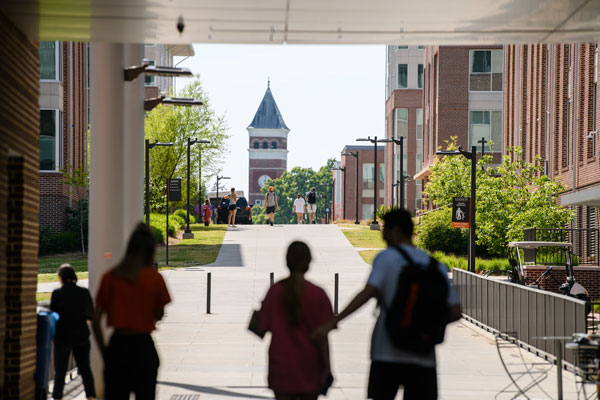 Students walk along the sidewalk in Douthit Hills with Old Main in the distance. 