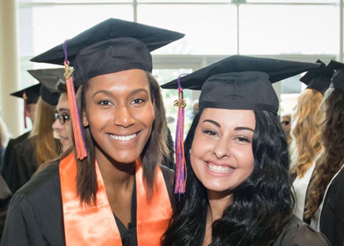 Two graduates smile in their regalia