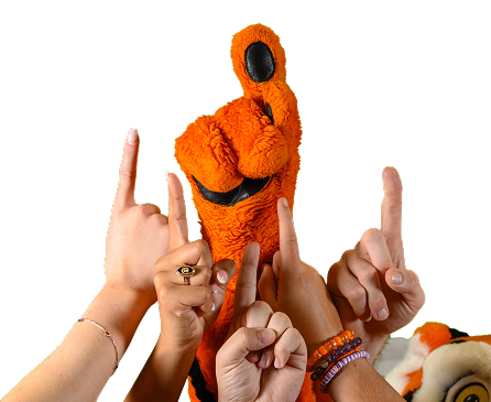 Five hands raised pointing their pointer fingers to the sky along side the Clemson tiger mascot who is doing the same.