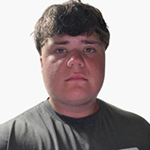 Head-and-shoulders portrait of a young man with short brown hair wearing a dark T-shirt against a plain white background.