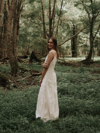 A woman in a white dress stands in a lush green forest, smiling softly.