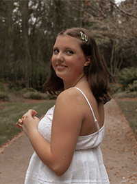 A woman in a white dress looks over shoulder in a forest environment. 