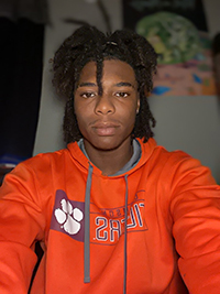 A young man wearing an orange hoodie with a paw print design, posing for a self portrait in a casual indoor setting.