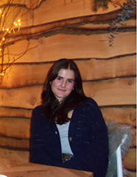 A woman sitting at a table in a cozy setting with wooden walls and warm lighting.