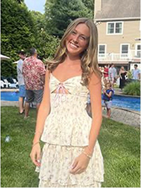 A young woman poses happily in a floral dress at a garden party near a swimming pool.