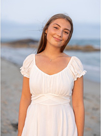 Young woman smiling on a beach at sunset, wearing a white dress.