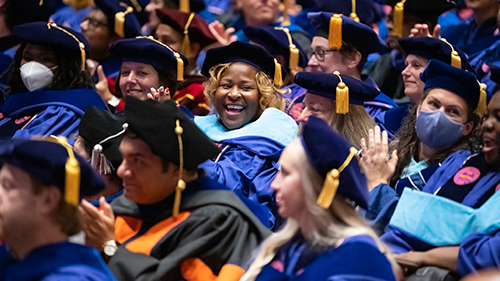 A joyful group of graduates in blue academic regalia and caps, celebrating during a commencement ceremony.
