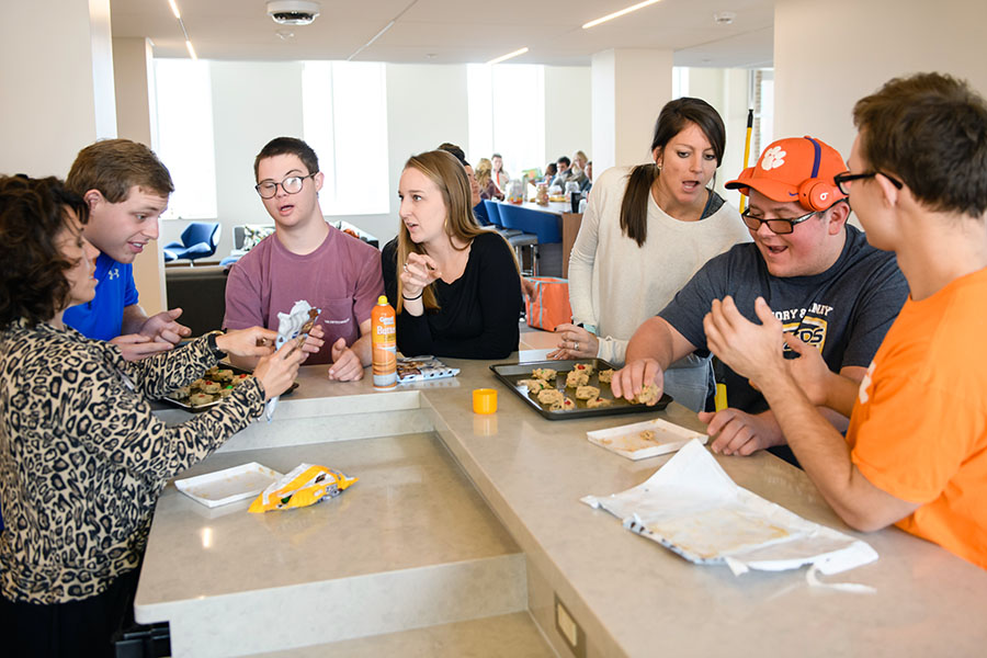 A group of young adults engaged in a lively conversation while sharing food at a communal table in a bright, modern space.