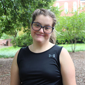 A young woman smiles while sitting outdoors in a garden setting.