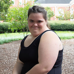 A young woman smiles while sitting outdoors in a garden setting.