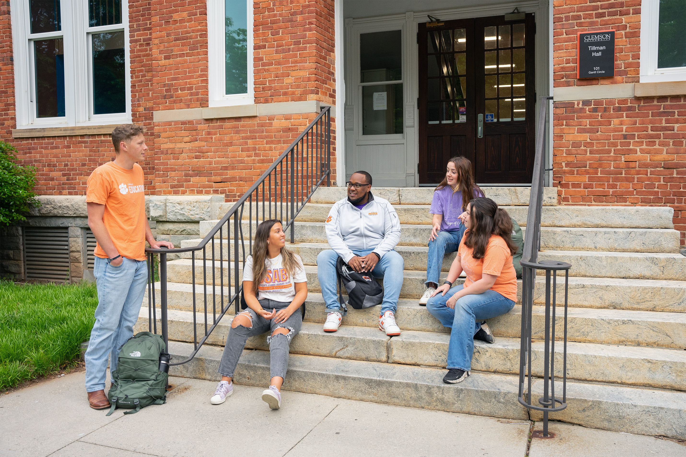 Students sit on steps outside of an academic building wearing orange and purple attire.